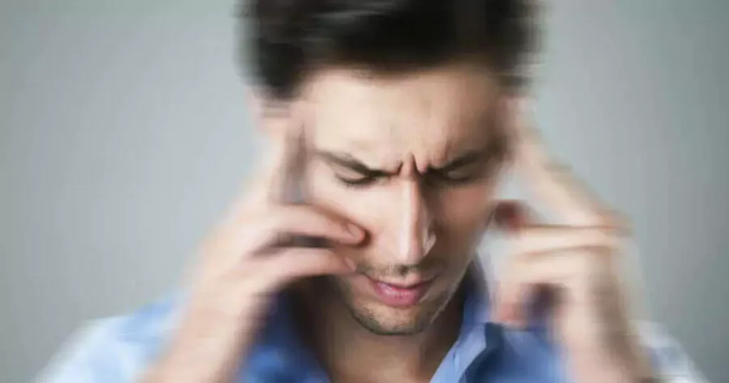 A man with a pained expression holds his head with both hands, indicating discomfort or distress