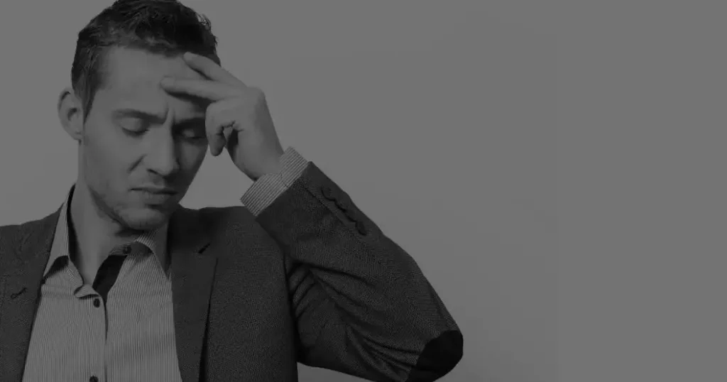 A man dressed in a suit holds his head, suggesting frustration or contemplation